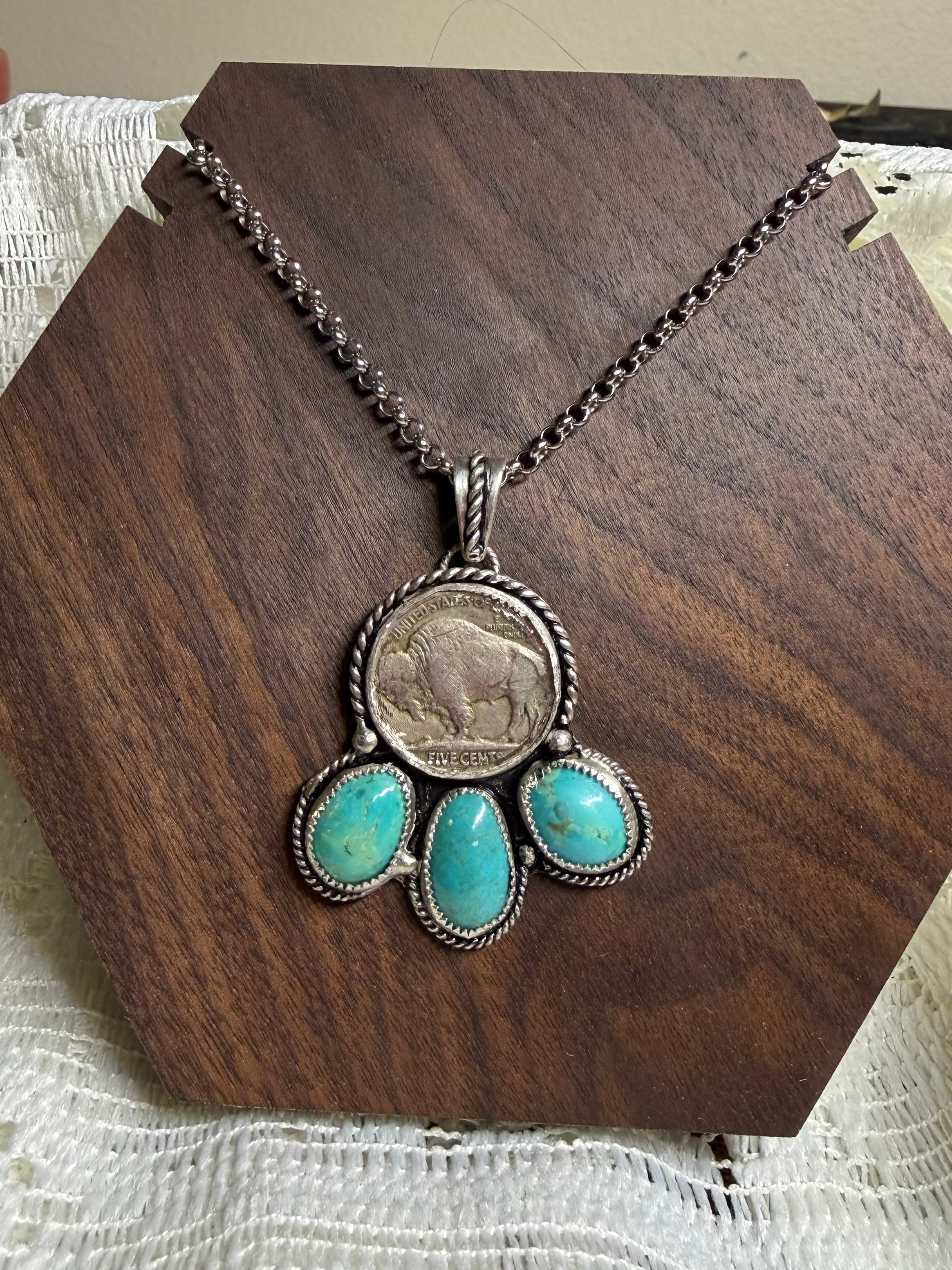 Necklace with turquoise stones and a coin pendant on a wooden stand